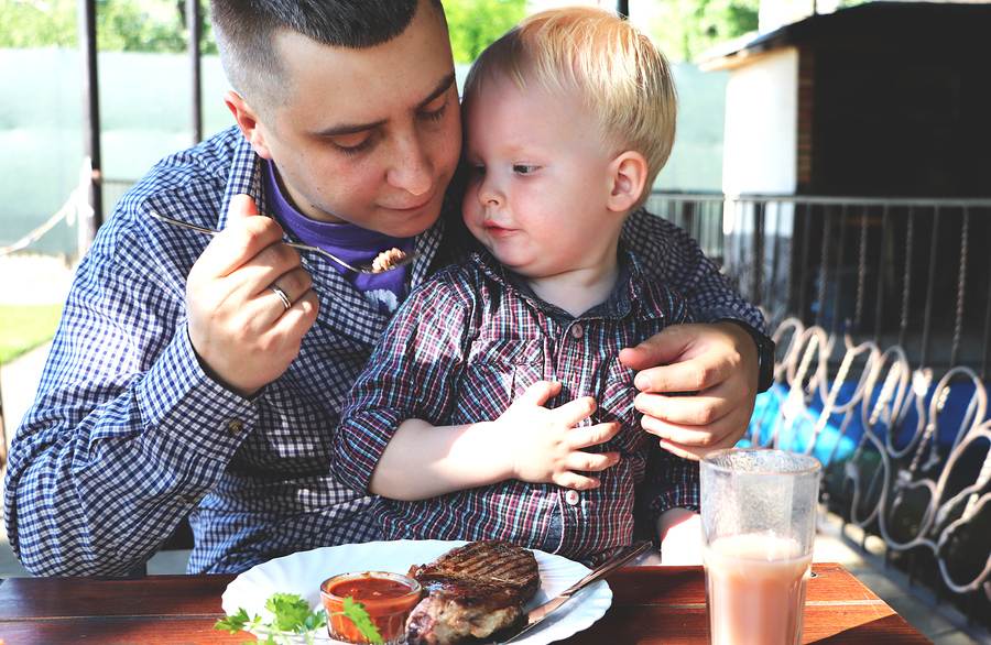 vader eet vlees in een restaurant met zijn zoontje op zijn schoot
